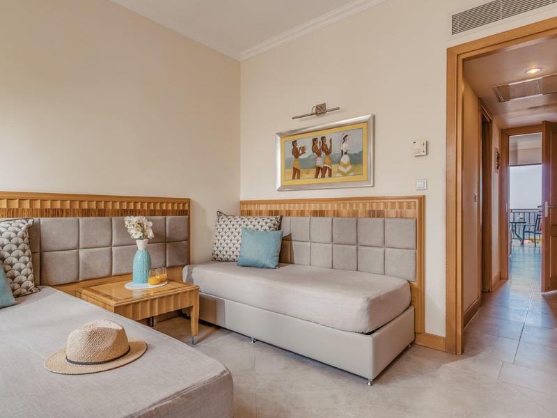 Helles Wohnzimmer mit beigen Sofas, Holztisch, bunten Kissen und Flur zum Balkon im Hintergrund.