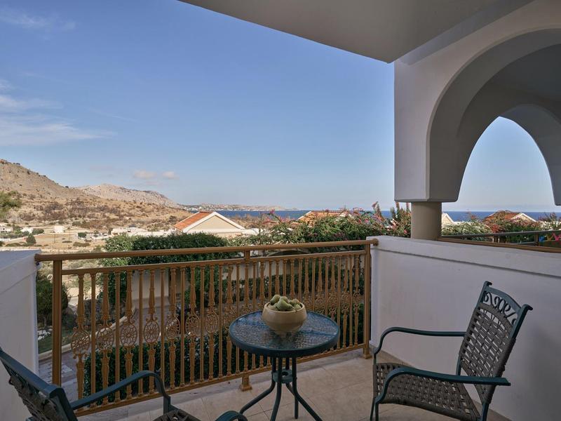 Balkon mit Tisch und Stühlen, Blick auf Landschaft und Meer unter blauem Himmel.