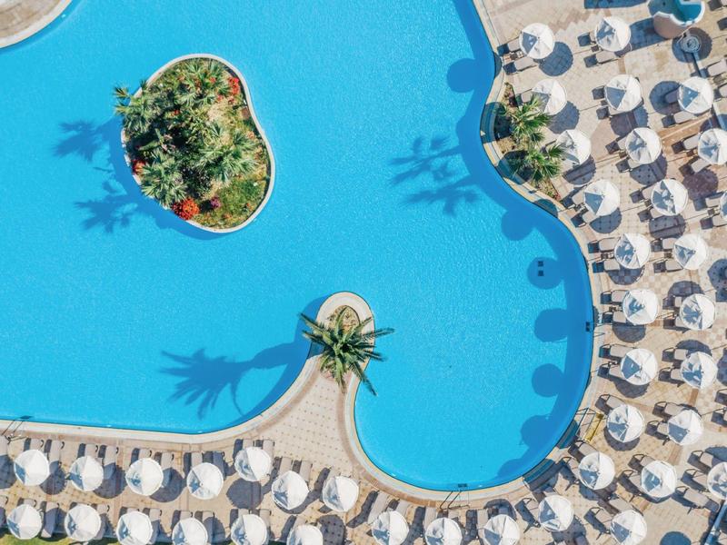 Vogelperspektive eines Pools mit Sonnenliegen und Schirmen am Rand.