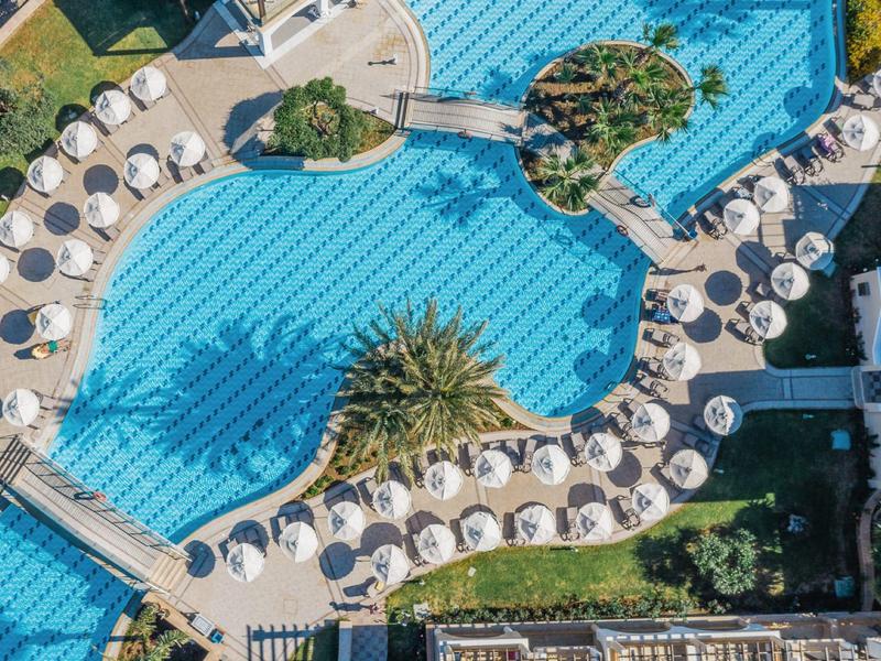 Vogelperspektive auf ein Resort mit geschwungenem Pool und Sonnenschirmen am Rand.