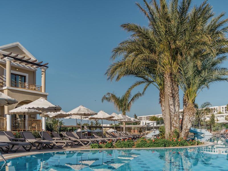 Hotelpool mit Liegestühlen und Palmen unter klarem blauem Himmel.