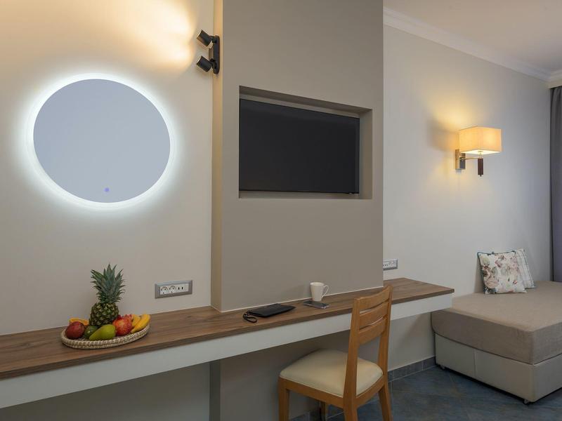 Modernes Hotelzimmer mit Schreibtisch, Stuhl, beleuchtetem Spiegel und gemütlicher Sitzecke.