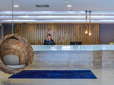 Reception d'hotel moderna con sedia sospesa in rattan e receptionist sullo sfondo.