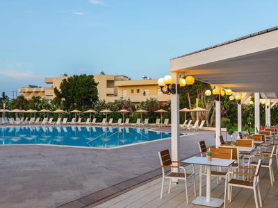 Piscina con lettini e terrazza esterna con tavoli e sedie in un complesso alberghiero