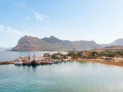 Küstenlandschaft mit klarem Wasser, Hafen und Bergen im Hintergrund.