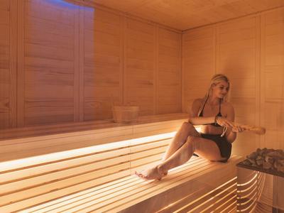 Frau entspannt sich allein in einer hellen Sauna mit Holzwänden und -bänken.