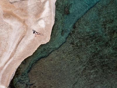 Luftaufnahme eines Strandes mit Sand, Wasser und einer Person mit Sonnenschirm.