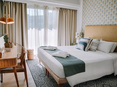 Helles Hotelzimmer mit großem Bett, Schreibtisch und Teppichboden.