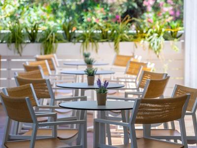 Leere Tische und Stühle auf einer Terrasse mit Pflanzen im Hintergrund.