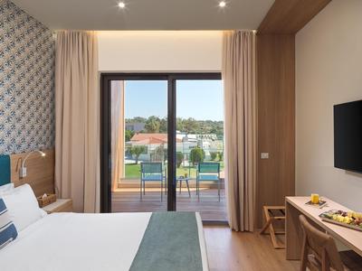 Modernes Hotelzimmer mit Doppelbett, Schreibtisch und Balkon mit Blick auf die Landschaft.