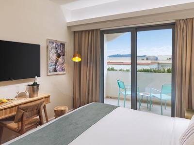 Modernes Hotelzimmer mit Bett, Schreibtisch und Balkon mit Sitzgelegenheit und Meerblick.
