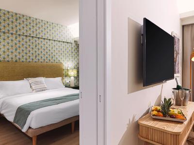 Modernes Hotelzimmer mit Bett, TV und frischem Obst auf einem Holztisch