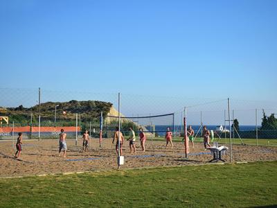 Persone che giocano a pallavolo su un campo di sabbia sotto un cielo sereno accanto a un hotel.