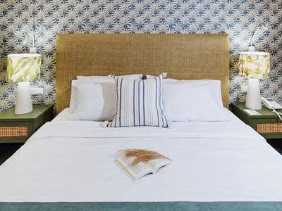 Modernes Bett mit weißen Laken, Kopfteil in Naturfarbe und zwei Nachttischen mit Lampen.