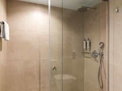 Moderne begehbare Dusche mit Glasabtrennung und braunen Fliesen in einem Hotelbad.