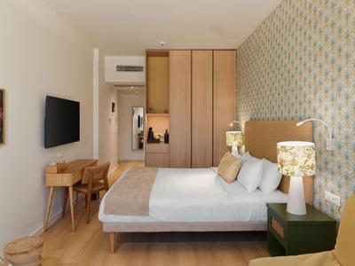 Modern eingerichtetes Hotelzimmer mit Doppelbett, Schreibtisch, TV und Tapete mit floralem Muster.