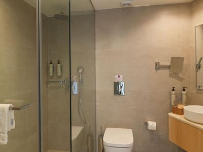 Modernes Badezimmer mit Glasdusche, WC, Waschbecken und hellen Fliesen.