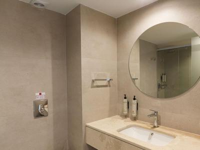 Modernes Hotelbadezimmer mit runder Wandspiegel, Waschbecken und Duschkabine.
