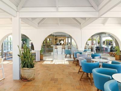 Hell eingerichteter Hotel-Loungebereich mit weißen Bögen, blauen Sesseln und Pflanzen.