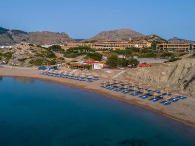Strand mit blauen Liegestühlen vor einem Hotel in einer bergigen Landschaft.