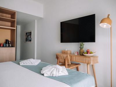 Modernes Hotelzimmer mit Fernseher, Schreibtisch, Stuhl und stehendem Lampenschirm.