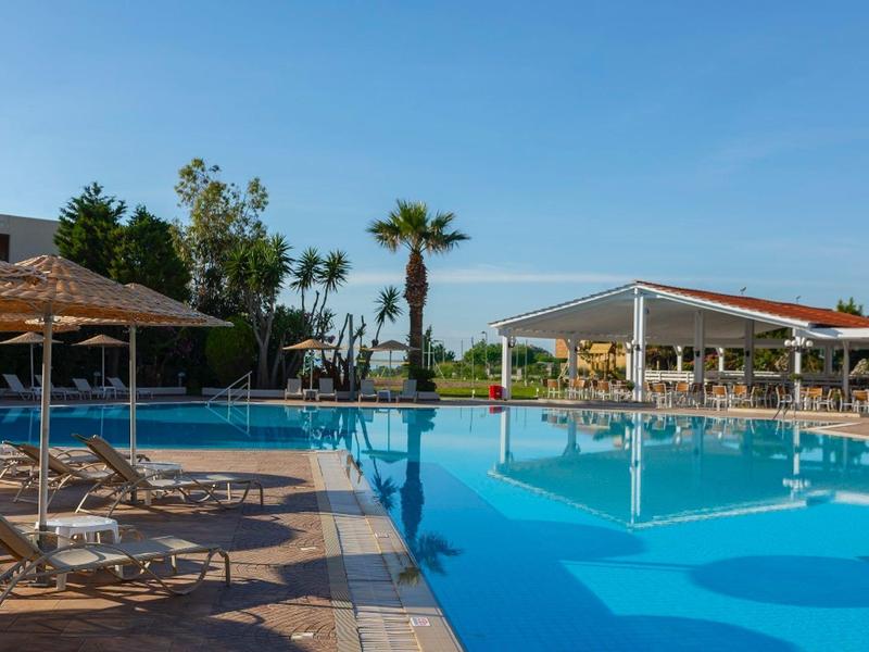 Ein großer Swimmingpool mit Sonnenliegen und Sonnenschirmen unter blauem Himmel.