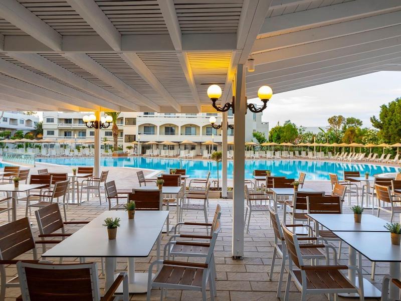 Offener Restaurantbereich mit Holztischen und Blick auf einen Hotelpool.