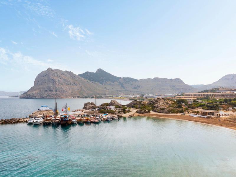 Küstenlandschaft mit klarem Wasser, Hafen und Bergen im Hintergrund.