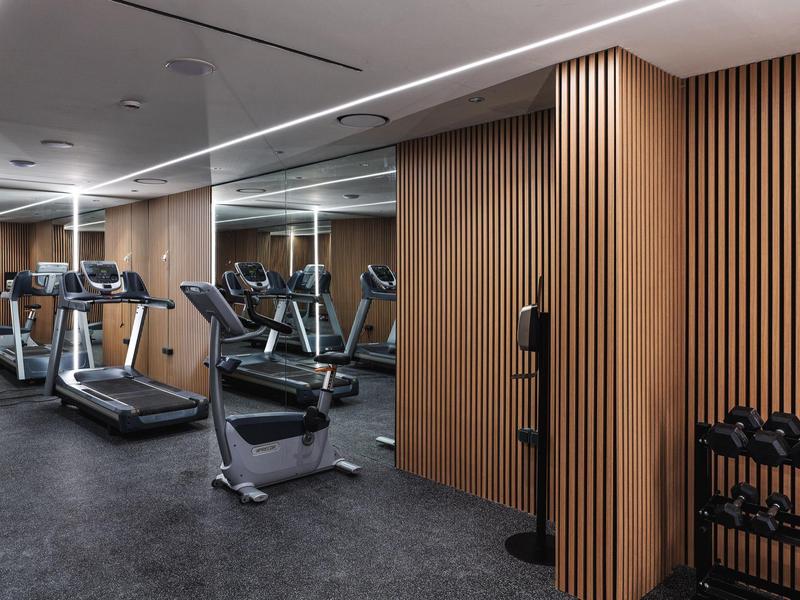 Moderner Fitnessraum mit Laufbändern, Gewichten und Holzpaneelen an der Wand.