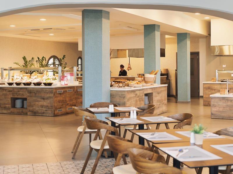 Moderner Restaurantinnenraum mit Holztischen und Stühlen, Buffetbereich und Stützsäulen.