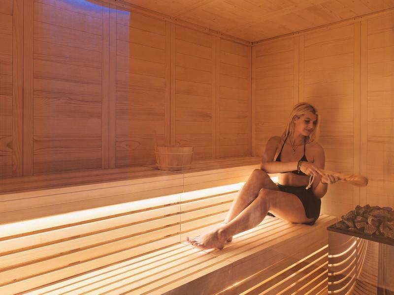 Frau entspannt sich allein in einer hellen Sauna mit Holzwänden und -bänken.