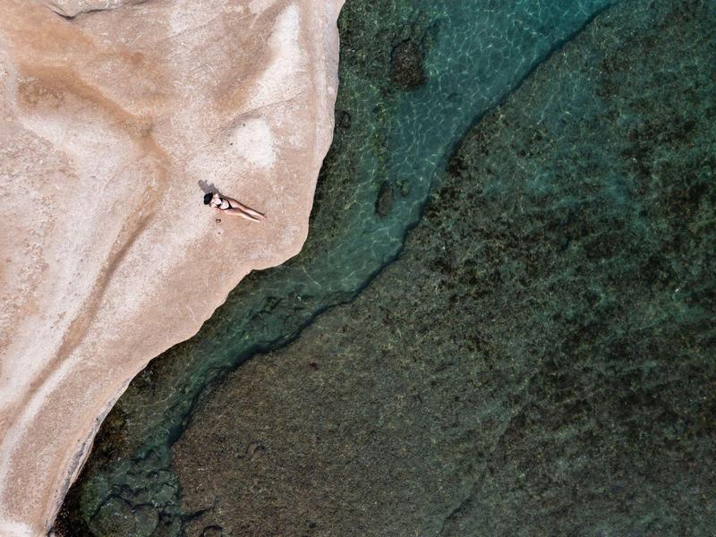 Luftaufnahme eines Strandes mit Sand, Wasser und einer Person mit Sonnenschirm.