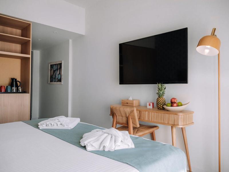 Modernes Hotelzimmer mit Fernseher, Schreibtisch, Stuhl und stehendem Lampenschirm.