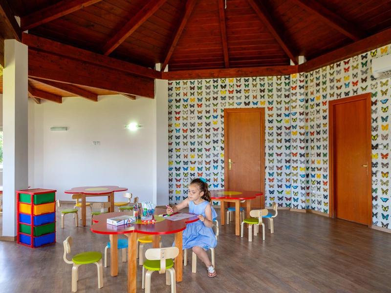 Kind spielt alleine in einem bunten Spielzimmer mit Tischen und Stühlen.