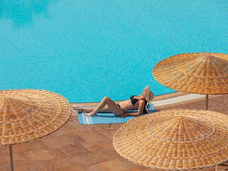 Person entspannt sich auf Liegestuhl neben großem blauen Pool mit Sonnenschirmen.