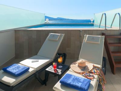 Twee ligbedden met handdoeken, drankjes en een zonnehoed op een zonnig terras met uitzicht op zee.