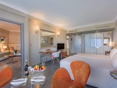 Ruime hotelkamer met bed, zithoek, moderne inrichting en glazen kledingkast.