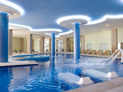 Overdekt zwembad met blauwe zuilen, watervallen en ligstoelen in een hotel.