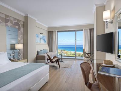 Lichte hotelkamer met zeezicht, moderne meubels en groot raam naar het terras.