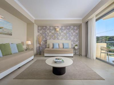 Licht ingericht hotelkamer met bank, bed, tafel en balkon met uitzicht.