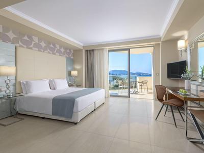 Moderne hotelkamer met groot bed, bureau en balkon met uitzicht op zee.