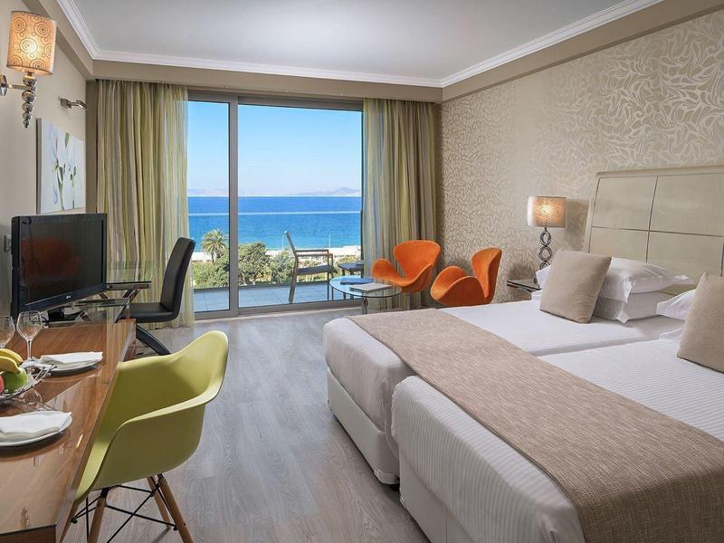 Moderne hotelkamer met twee eenpersoonsbedden, een bureau, stoelen en een balkon met uitzicht op zee.