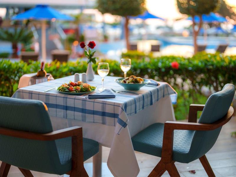 Buitentafel voor twee met eten en drinken, uitzicht op tuin en zwembadgebied.