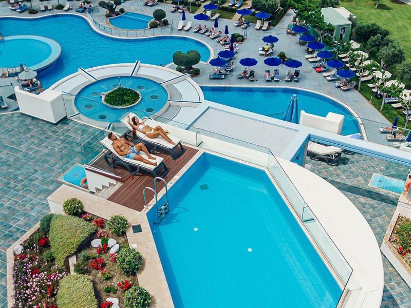 Een groot buitenzwembad met ligbedden en aangelegde tuinen bij een resort.