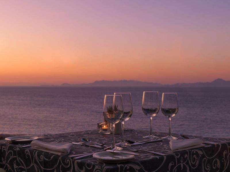 Tafel met wijnglazen aan zee bij zonsondergang met paars-oranje lucht