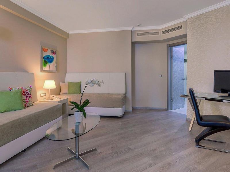 Moderne hotelkamer met twee bedden, een glazen tafel en een werkplek met computer.