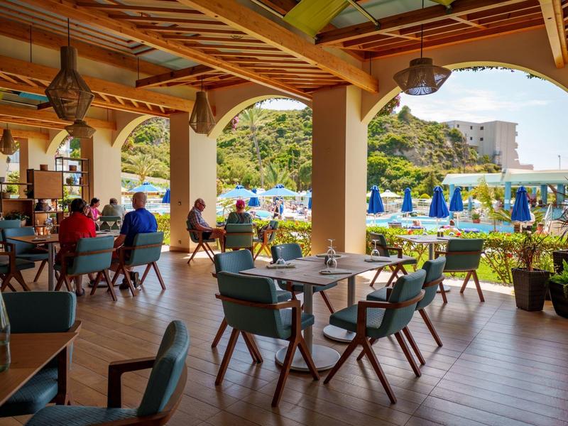 Overdekt terras met eettafels met uitzicht op zwembad en heuvels op de achtergrond.