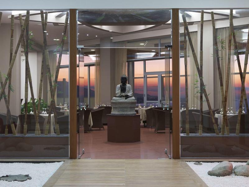 Hotel lounge met grote ramen met uitzicht op zonsondergang, met beelden en zithoeken.