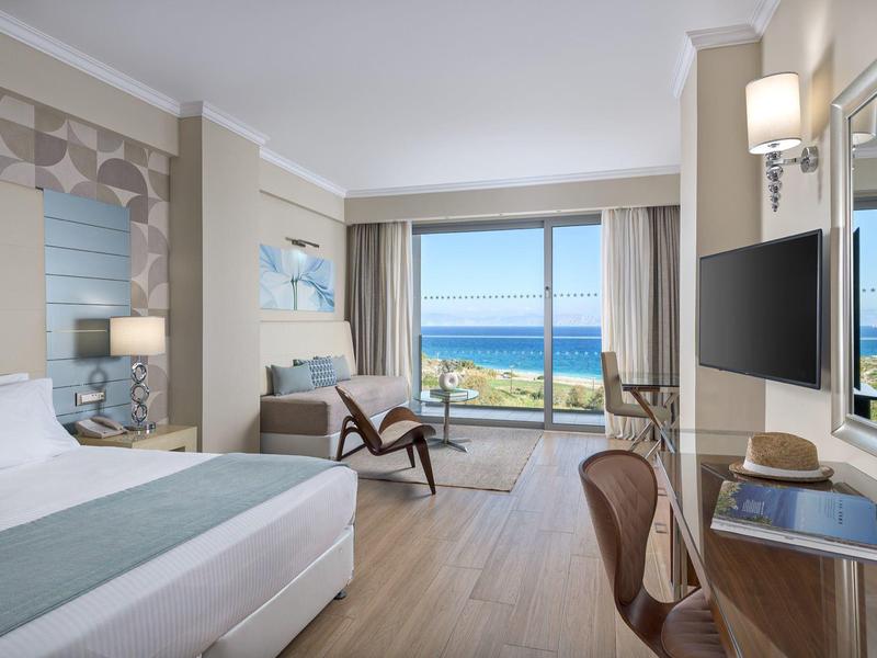 Lichte hotelkamer met zeezicht, moderne meubels en groot raam naar het terras.