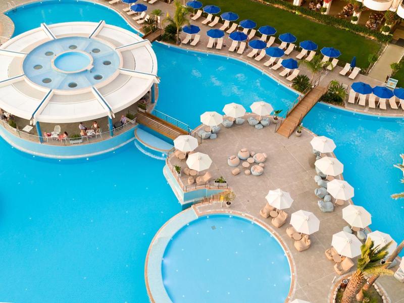 Área de piscina moderna con sombrillas y restaurante circular sobre el agua.